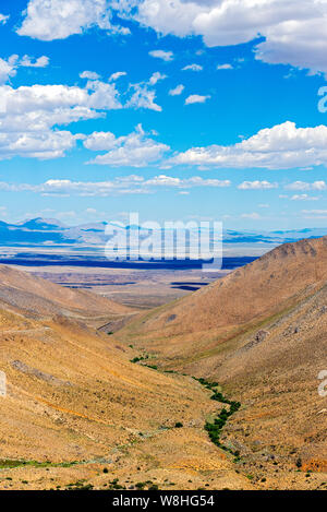 Blick über Canyon mit gold-braune Berge in das Tal hinaus unter strahlend blauen Himmel mit flauschigen weissen Wolken. Stockfoto