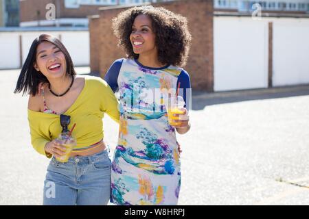 Zwei junge Frauen mit Getränken im Freien, Lachen. Stockfoto