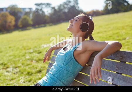 Junge Frau Musikhören von Smart Phone, auf einer Bank sitzen. Stockfoto
