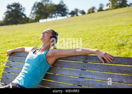 Junge Frau Musikhören von Smart Phone, auf einer Bank sitzen. Stockfoto