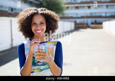 Junge Frau mit Getränk im Freien, ein Lächeln auf den Lippen. Stockfoto