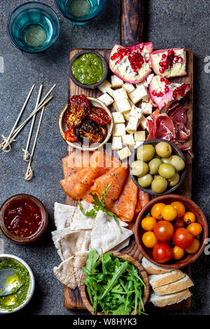 Antipasti. Wein Set Vorspeise. Schinken Serrano, geräucherten Lachs, getrocknete und frische Tomaten, Olivenöl, Käse, Wein an Bord. Ansicht von oben, grau cncrete Hintergrund. Stockfoto