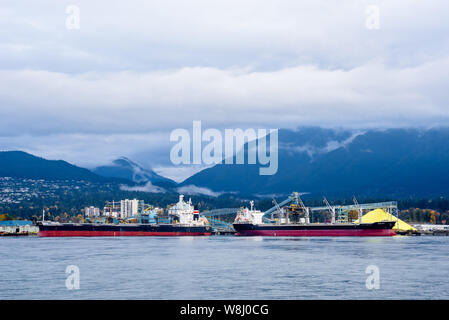 VANCOUVER, BC, Kanada - 30. OKTOBER 2018: Zwei Frachtschiffe sind in Vancouver Hafen angedockt, vor der nahe gelegenen Berge. Stockfoto