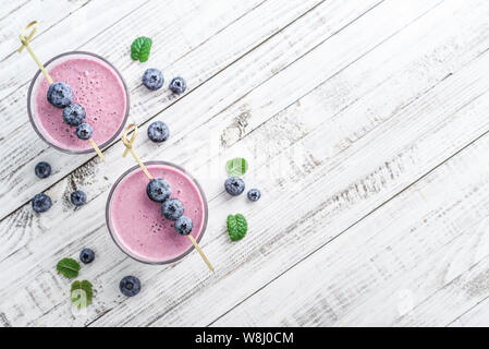 Blueberry Smoothie in Glas mit frischen Beeren und Minze auf weißem Holz- Hintergrund, Ansicht von oben Stockfoto