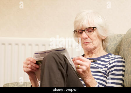Ältere ältere Frau halten Geist aktiv tun ein Kreuzworträtsel anti-age alte Geist uk zu helfen Stockfoto