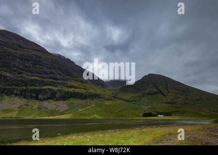 Eine malerische Landschaft von einem entfernten Haus durch ein Loch (Loch Achtriochtan) und Berge in Glencoe, die schottischen Highlands Stockfoto