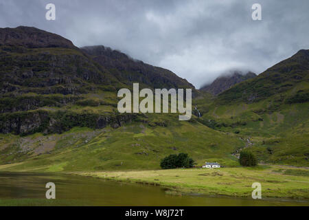 Eine malerische Landschaft von einem entfernten Haus durch ein Loch (Loch Achtriochtan) und Berge in Glencoe, die schottischen Highlands Stockfoto