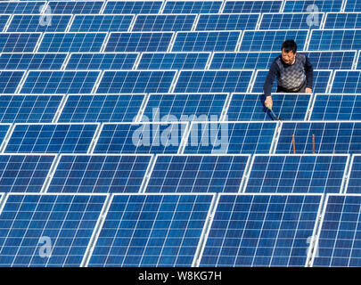 ---- Ein chinesischer Arbeiter Stäube aus Sonnenkollektoren mit einer Photovoltaik- Kraftwerk in Baokang Maqiao Stadt, Grafschaft, Xiangyang City, Central China Hubei Stockfoto