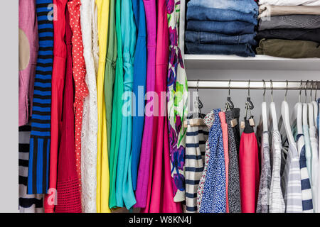 Mode Kleidung in begehbaren Kleiderschrank oder Store Display für den Einkauf angezeigt. Bunte Auswahl an trendigen Outfits auch in sauberen Regale angeordnet. Frühjahrsputz Konzept. Sommer home Wohnzimmer Schrank. Stockfoto