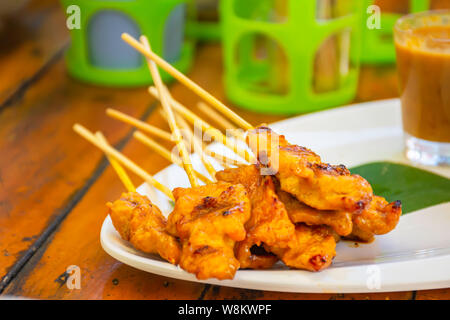 Schwein Satay mit Kokosmilch mit Sauce aus weißem Kunststoff Platte auf dem Holztisch. Stockfoto