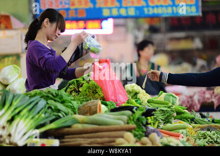 ---- Ein chinesischer Hersteller setzt Gemüse in einer Wegwerf- Tasche auf einem freien Markt in Qingdao Stadt, East China Provinz Shandong, 28. Mai 2013. Ein comme Stockfoto