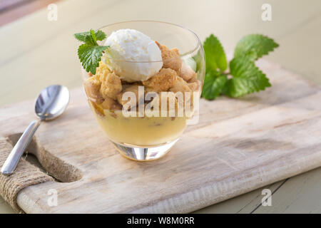 Apple Crumble topping Vanilleeis mit Melisa in Glas und Holz- fach am Tisch serviert. Stockfoto