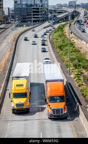 Zwei verschiedene Modelle von Big Rig orange und gelb semi Trucks mit trockenen Van und Kühlschrank Auflieger laufen vor einer anderen Verkehr auf der r Stockfoto