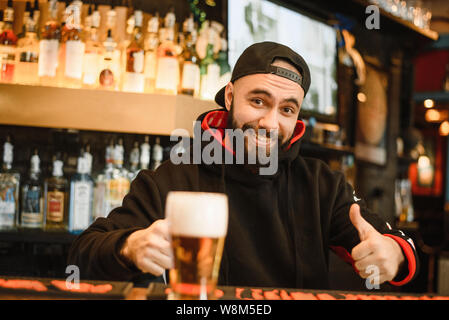 Lächelnd bärtigen Barkeeper gibt Bier in ein Glas. Freundliche Mann an der Bar arbeiten. Stockfoto