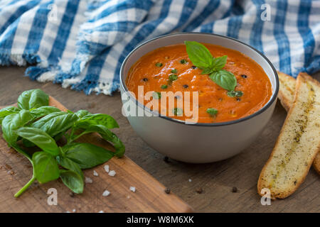 Eine Schale mit frischen Tomaten Suppe aus weisser Keramik Schüssel, garniert mit Basilikum, Croutons, würzen und ein wenig Öl, und serviert mit knusprigem Brot. Stockfoto