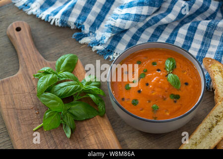 Eine Schale mit frischen Tomaten Suppe aus weisser Keramik Schüssel, garniert mit Basilikum, Croutons, würzen und ein wenig Öl, und serviert mit knusprigem Brot. Stockfoto
