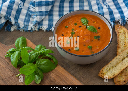 Eine Schale mit frischen Tomaten Suppe aus weisser Keramik Schüssel, garniert mit Basilikum, Croutons, würzen und ein wenig Öl, und serviert mit knusprigem Brot. Stockfoto