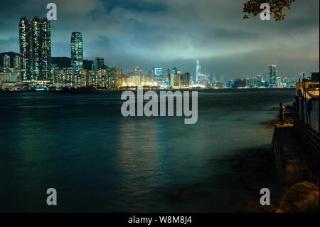 Ein Mann Fische auf der Bank in Lei Yue Mun Dorf in der Nacht mit Bürogebäude im Victoria Hafen im Hintergrund in Hongkong, China, Dezember Stockfoto