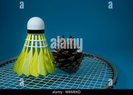 Gelb gefiederten Federball und Pine Cone auf Badminton Schläger auf blauem Hintergrund in der Nähe zu sehen. Stockfoto