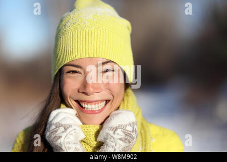 Winter Mädchen lächelnd draußen im Schnee. Portrait der asiatischen Frau glücklich verspielt im Freien mit gesunden Lächeln auf sonnigen Winter Tag tragen gelbe Oberbekleidung beanie Strick Mütze und Handschuhe. Stockfoto