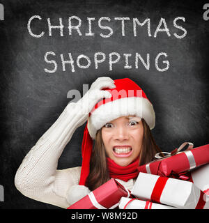Weihnachten Geschenke Shopping Frau Urlaub stress. Betonte Mädchen Geschenke zu kaufen tragen rote Weihnachtsmütze suchen frustriert und verzweifelt mit lustigen Ausdruck auf Schwarze Schiefertafel copyspace Hintergrund. Stockfoto