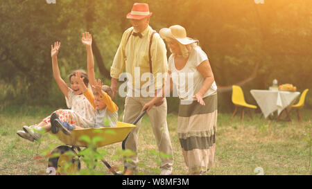 Oma und Opa drängen ihre Enkelkinder in einer Schubkarre Stockfoto