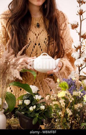 Stillleben mit Blumen und Weidenruten. Eine Teekanne mit duftenden Kaffee in der Hand. Dekor. Dekorationen, Kerzen, chemische Weidenzweige und eine Weiblich Stockfoto