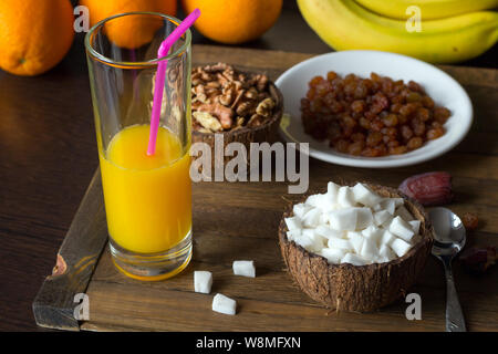 Leckere rohe Diät Frühstück auf Holztisch. Coconut Fleisch und Kerne von Walnut in Schalen aus Kokosnussschalen. Ein Glas frisch gepressten Orangensaft Stockfoto