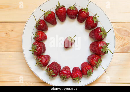 Erdbeeren sind in der Form eines Kreises auf einem weißen Teller. Eine kleine Beere rechts in der Mitte. Leckere natürliche Dessert. Blick von oben. Brig Stockfoto