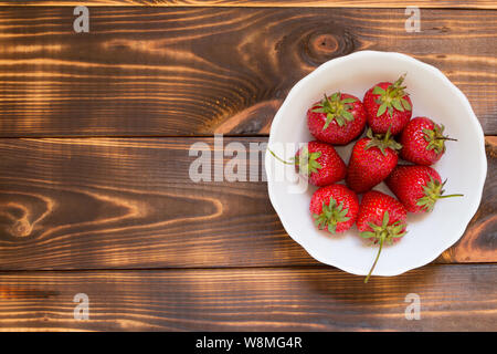 Saftige rote Erdbeeren in Weiß Schüssel auf Holz- Hintergrund mit Kopie Raum auf der linken Seite. Ansicht von oben. Close-up. Köstliches Dessert. Sommer Ernte. Lecker n Stockfoto