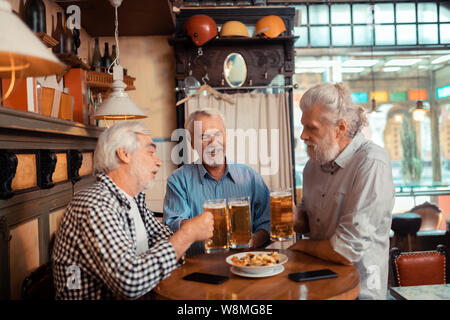 Drei pensionierte Männer essen Snacks und Bier trinken. Stockfoto
