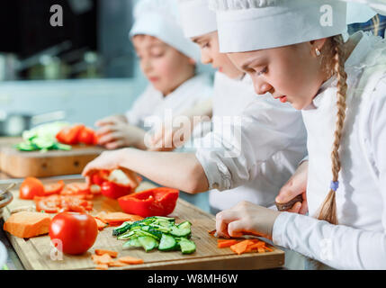 Kinder in Kochmütze schleifen Gemüse in der Küche. Stockfoto