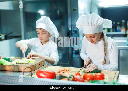 Kinder in Kochmütze schleifen Gemüse in der Küche. Stockfoto