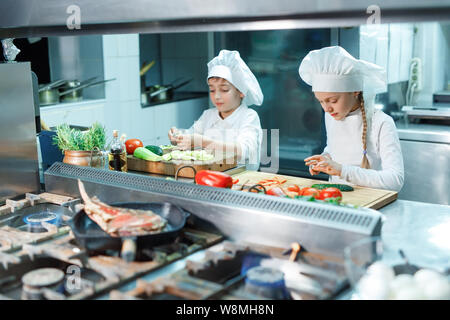 Kinder in Kochmütze schleifen Gemüse in der Küche. Stockfoto