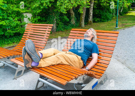 Ein Männer mittleren Alters entspannen auf einer hölzernen Schaukelstuhl im öffentlichen Park. Stockfoto