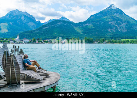 Ein Männer mittleren Alters Entspannen auf einem hölzernen Liegestuhl Lake St. Wolfgang in der Nähe von Strobl in Österreich Stockfoto