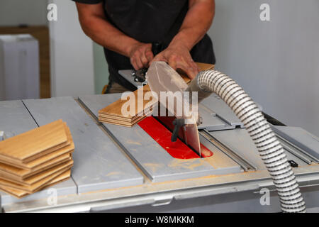 Der Arbeitnehmer schneidet den Parkettboden manuell auf einer Kreissäge, und das Sägemehl fliegt Stockfoto