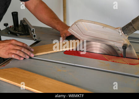 Der Arbeitnehmer schneidet den Parkettboden manuell auf einer Kreissäge, und das Sägemehl fliegt Stockfoto