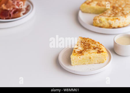 Tortilla, spanisches Omelette mit Eiern und Kartoffeln gemacht. Traditionelle spanische Tapas serviert mit Scheiben von jamon, iberischen Schinken auf weißem Hintergrund. Stockfoto