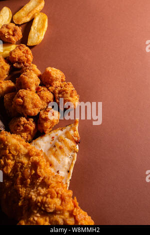 Knusprig gebratene Hähnchen und Pommes Frites gegen braunen Hintergrund Stockfoto