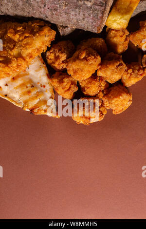 Knusprig gebratene Hähnchen und Pommes Frites gegen braunen Hintergrund Stockfoto