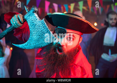 Portrait von fröhlichen bärtigen Männer gekleidet wie ein Pirat auf einer Halloween Party. Mann in einem Dracula Kostüm im Hintergrund. Stockfoto