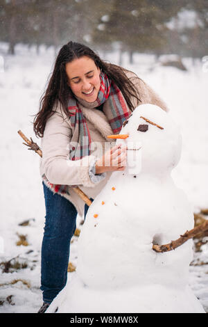 Portrait einer liebenswerten Frau in einem Mantel bekleidet, eine Karotte Nase auf einen Schneemann - Ferienhäuser Konzept - Bild vertikal Stockfoto