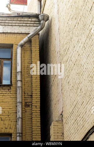 Drainagerohr verlegt auf einem gelben Wand. Der Innenhof des alten Hauses. Über Architektur, Kanalisation, Kommunikation. Stockfoto