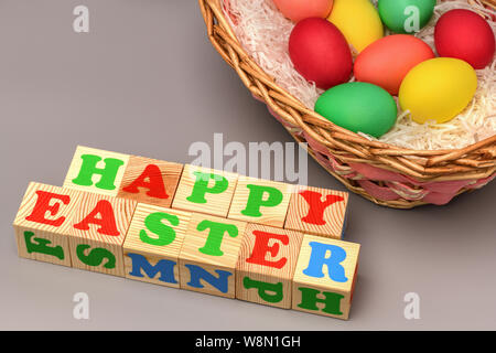 Korb mit bunten Ostereier und Aufschrift Würfel Frohe Ostern auf grauem Hintergrund. Horizontale Fotografie Stockfoto