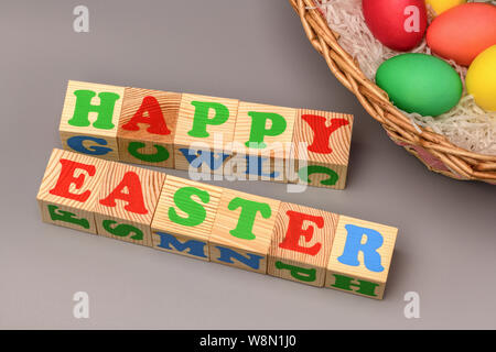Korb mit bunten Ostereier und Aufschrift Würfel Frohe Ostern auf grauem Hintergrund. Horizontale Fotografie Stockfoto