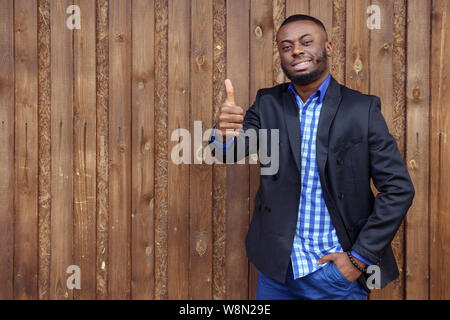 Afro-amerikanische Geschäftsmann in Hemd und Anzug Jacke. Schwarz lächelnden Mann zeigt Geste Daumen oben auf dunklen Hintergrund. Sieger Konzept. Stockfoto