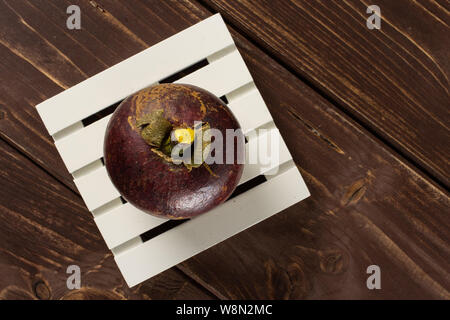 Ein ganzes deep purple Mangosteen auf weißen Palette flatlay auf braunem Holz Stockfoto