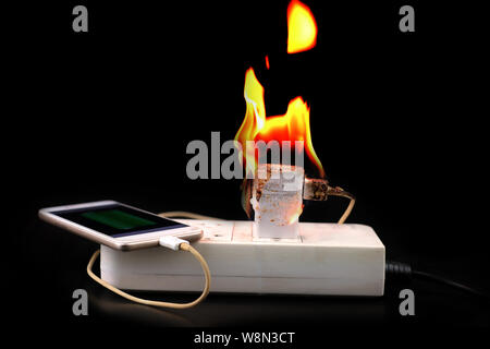 Auf Feuer Adapter Smart Phone Charger an Stecker in Steckdose auf schwarzem Hintergrund Stockfoto