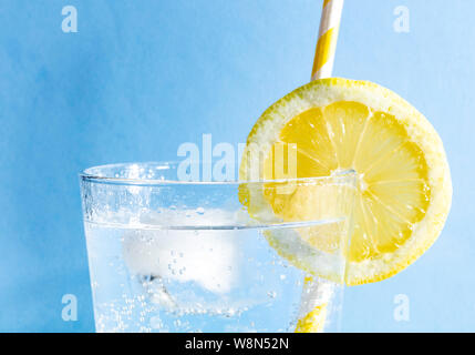 Frische Getränk mit bubles ein Ice Cube, einer Scheibe Zitrone und ein Stroh auf einem blauen Hintergrund Stockfoto